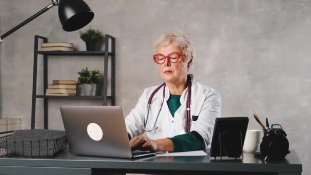 Médico femenino de mediana edad usando portátil, escribiendo notas con estetoscopio en la mesa. Concepto de salud. Médico médico escribiendo y tomando notas — Vídeos de Stock