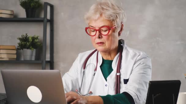 中世の女性医師はノートパソコンを使用して、テーブルの上に聴診器でノートを書きます。医療の概念。医師がノートを書き取る — ストック動画