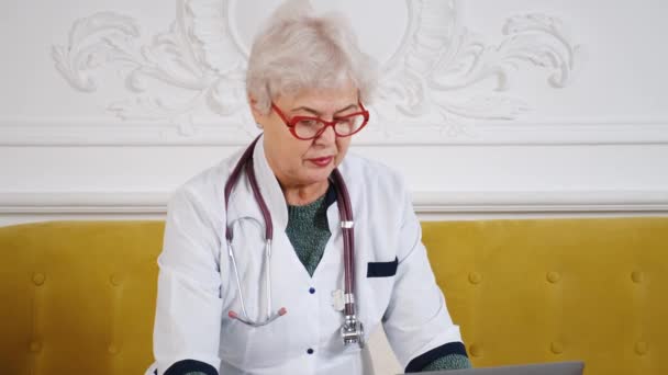 Médica de meia idade usando laptop, escrevendo notas com estetoscópio na mesa. Conceito de saúde. Médico médico escrever e tomar notas — Vídeo de Stock