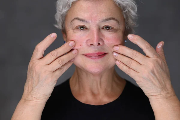 Portrait of Beautiful Senior Woman gently Applying Under Eye Face Cream. Elderly Lady Makes Her Skin Soft, Wrinkle Free with Natural anti-aging Cosmetics — Stock Photo, Image