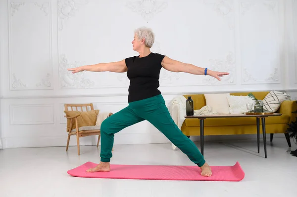 Eine schön aussehende alte Frau macht Yoga zu Hause in einem schönen weißen Interieur — Stockfoto