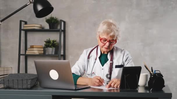 Seorang dokter wanita paruh baya berbicara kepada pasien konferensi video. Telemedicine, konsultasi pasien online — Stok Video