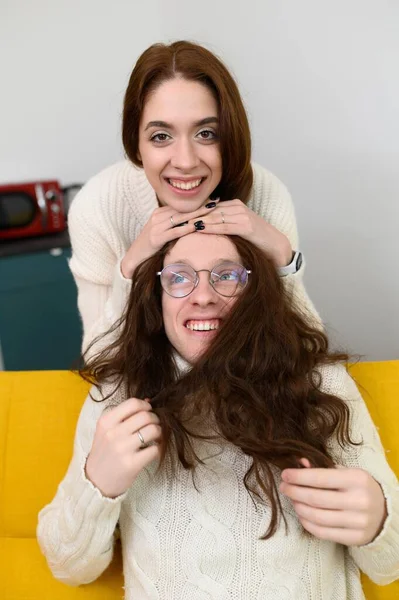 Um jovem casal passa um tempo em casa juntos. A brincar sentado no sofá. Um homem experimenta um cabelo de meninas — Fotografia de Stock