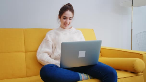 Retrato de uma mulher bonita usando um computador portátil, sentado na sala de estar em um apartamento. Uma pessoa alegre trabalha de casa, faz compras na Internet, negocia via comunicação por vídeo — Vídeo de Stock