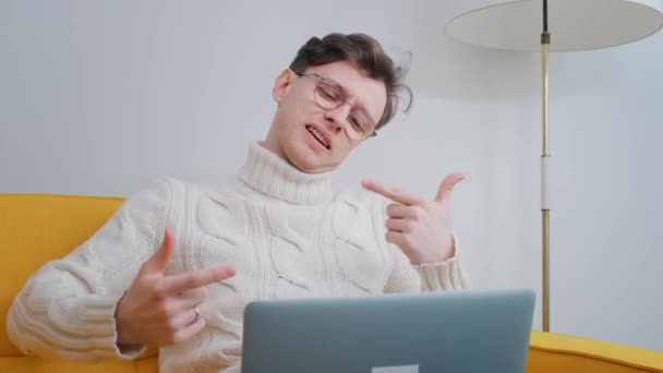 Portret van een knappe man met een bril, met behulp van een laptop computer, zittend in de woonkamer in een appartement. A Joyful Person Works from Home, doet aankopen op het internet — Stockvideo