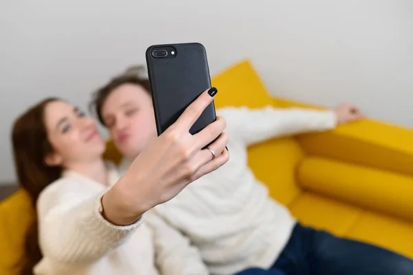 Positivo jovem casal tomando selfie enquanto sentado no sofá em casa — Fotografia de Stock