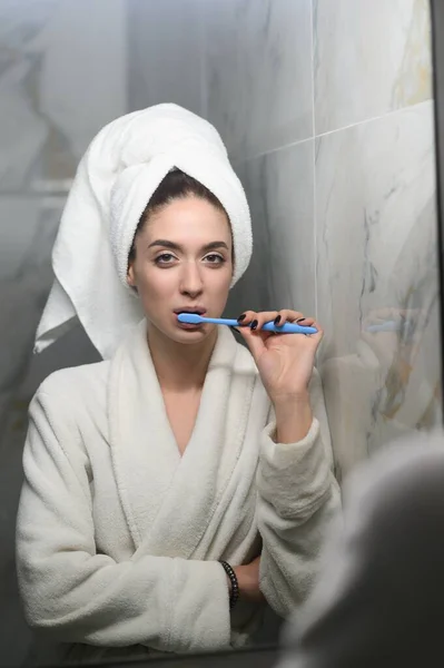 Fiatal, gyönyörű nő a fürdőszobában, fogat mos a tükör előtt. Stock Kép