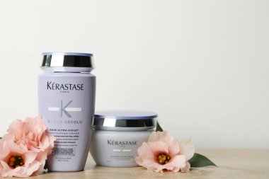 MYKOLAIV, UKRAINE - Eylül 07, 2021: Kerastase saç bakım kozmetik ürünleri ve ahşap masadaki güzel çiçekler. Metin için boşluk