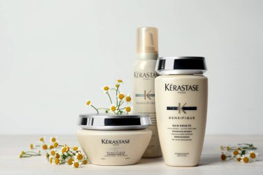 MYKOLAIV, UKRAINE - EYLÜL 07, 2021: Kerastase saç bakım kozmetik ürünleri ve beyaz ahşap masa üzerinde papatya çiçekleri