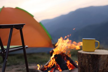 Açık havada şenlik ateşinin yanında, üzerinde sıcak içecek olan sarı bardak, mesaj için yer. Kamp sezonu