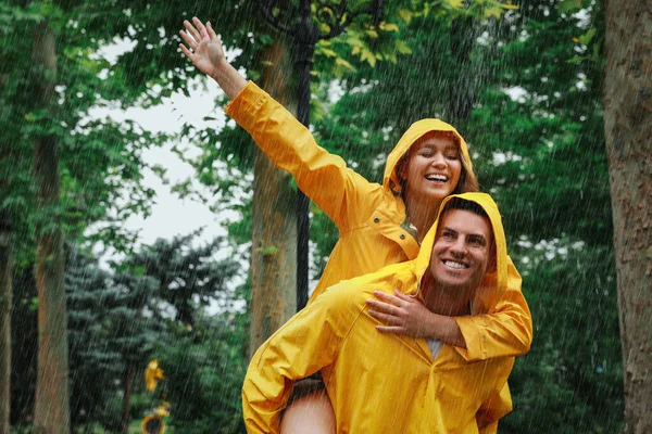 可爱的情侣和雨衣在公园里享受雨带来的乐趣 — 图库照片
