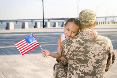 Asker ve küçük kızı Amerika bayrağıyla dışarıda kucaklaşıyorlar.