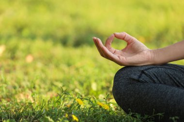 Yeşil çimenler üzerinde meditasyon yapan bir kadın, yakın plan. Metin için boşluk