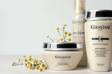 MYKOLAIV, UKRAINE - Eylül 07, 2021: Kerastase saç bakım kozmetik ürünleri seti ve beyaz ahşap masa üzerinde papatya çiçekleri. Metin için boşluk