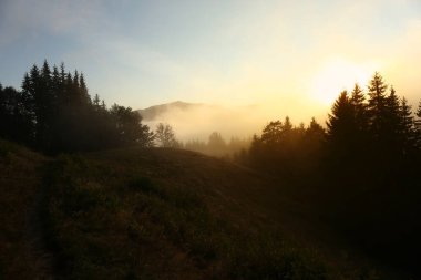 Güneşin doğuşunda sisle kaplı dağların resimli görüntüsü