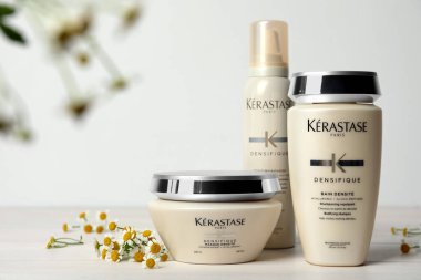 MYKOLAIV, UKRAINE - EYLÜL 07, 2021: Kerastase saç bakım kozmetik ürünleri ve beyaz ahşap masa üzerinde papatya çiçekleri