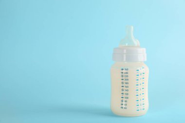 Açık mavi arka planda bebek mamasıyla beslenme şişesi, metin için boşluk. Bebek sütü