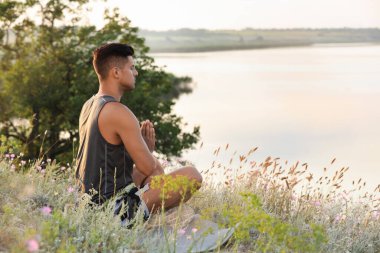 Nehir kenarındaki çayırda meditasyon yapan bir adam. Metin için boşluk
