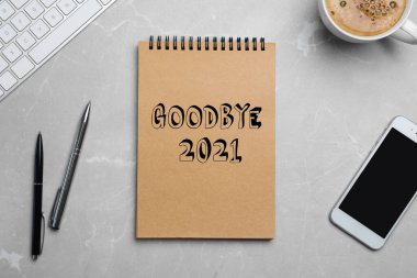 Cümleli not defteri Elveda 2021, akıllı telefon, klavye, kalemler ve kahve fincanı gri mermer masada, düz uzanmış 