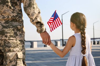 Asker ve Amerikan bayrağı taşıyan küçük kızı dışarıda el ele tutuşuyorlar. ABD 'de Gaziler Günü