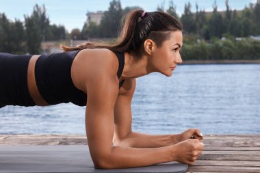 Nehir kenarındaki ahşap iskelede tahta egzersizi yapan genç bir kadın.