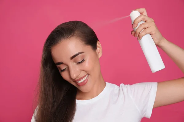 Young woman applying dry shampoo against pink background