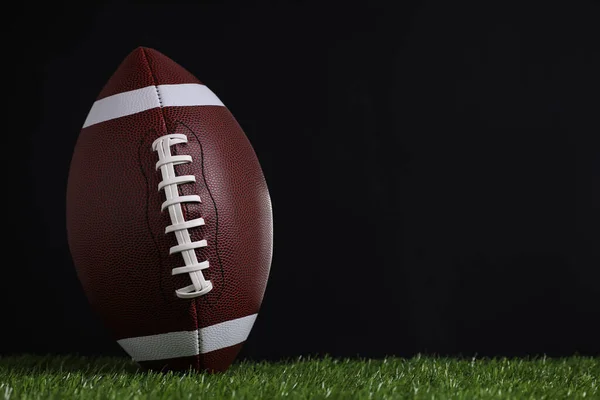 黒を背景に緑の芝生の上でアメリカンフットボールボール テキストのスペース — ストック写真