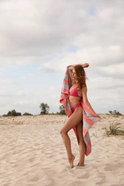 美しいです女性でビキニとともにビーチタオルオン砂 — ストック写真