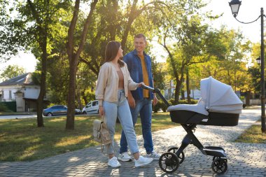 Mutlu ebeveynler güneşli bir günde bebekleriyle parkta yürüyorlar.
