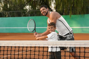 Baba oğluna kortta tenis oynamayı öğretiyor.