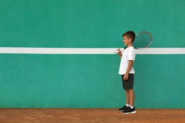 Tenis kortunda yeşil duvarın yanında şirin bir çocuk. Metin için boşluk