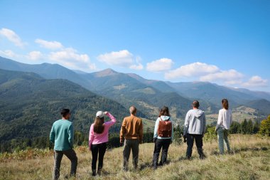 Bir grup insan dağlarda, arka planda birlikte vakit geçiriyorlar.