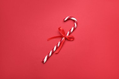 Kırmızı arka planda fiyonklu tatlı Noel şekeri bastonu.