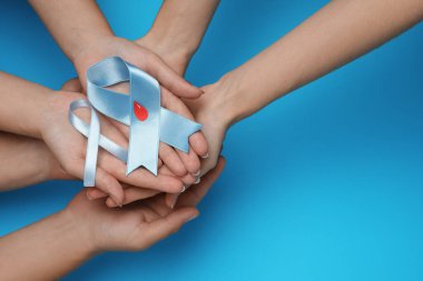 İnsanlar açık mavi kurdeleler tutuyor. Renk arkaplanında kağıt kan damlaları var. Üstten görünüş ve yazı için boşluk. Diyabet farkındalığı