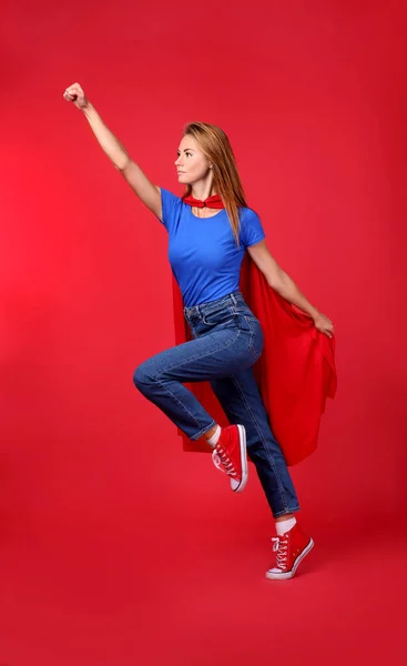 穿着超级英雄斗篷的自信女人在红色背景上跳跃 — 图库照片