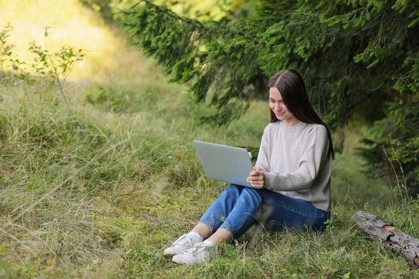 Young woman working on laptop in forest, space for text