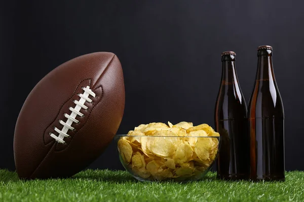 緑の芝生の上でポテトチップスやビールとアメリカのサッカーボール — ストック写真