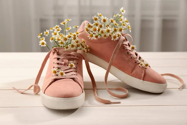 白い木製の表面に美しいカモミールの花を持つ靴 — ストック写真