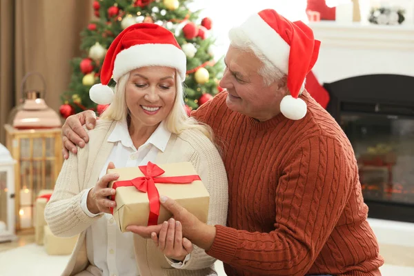 Happy mature man presenting Christmas gift to his wife at home
