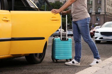 Elinde bavul olan bir adam şehirde taksiye biniyor.