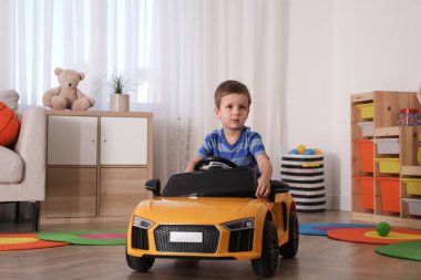 Küçük çocuk odada oyuncak arabayla oynuyor.