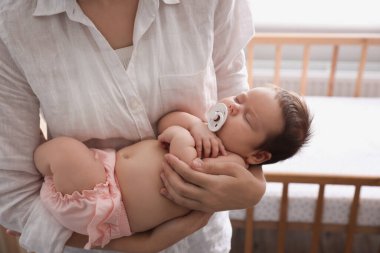 Anne küçük bebeğini emzik ile kucağında tutuyor, yakın plan.