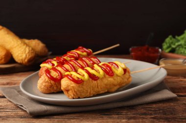 Tahta masada hardallı ve ketçaplı lezzetli mısırlı sosisli sandviç.