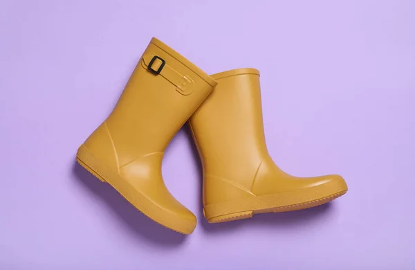 Pair of yellow rubber boots on violet background, top view