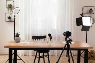 Odadaki masanın yakınındaki tripodlarda kamera ve ışıklandırma ekipmanları var. Blogger işyeri