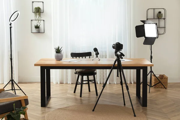 Camera and lighting equipment on tripods near table in room. Blogger workplace