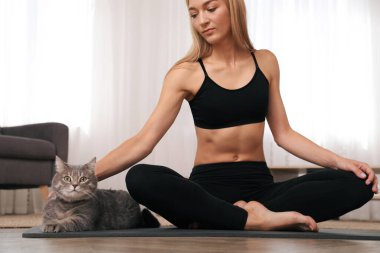 Evde yoga yaparken kedisini okşayan bir kadın.