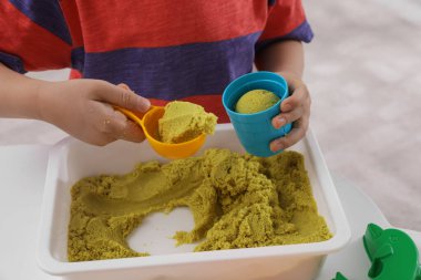Küçük çocuk içeride masada parlak kinetik kumla oynuyor, yakın plan.
