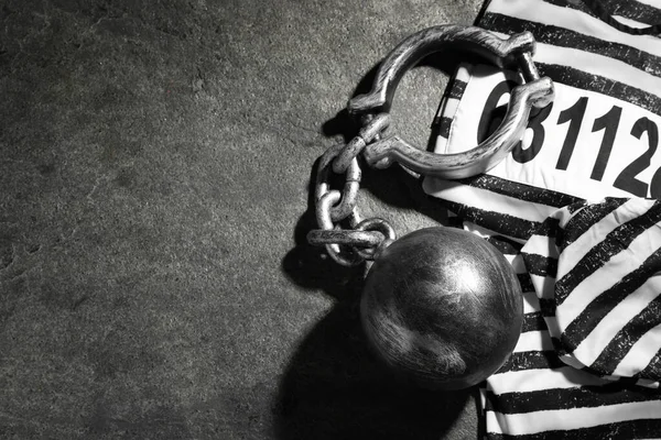 Prisoner ball with chain and jail clothes on grey table, flat lay. Space for text