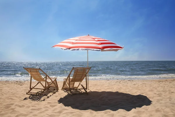 砂浜に赤と白の縞模様のビーチ傘の近くのデッキチェア — ストック写真